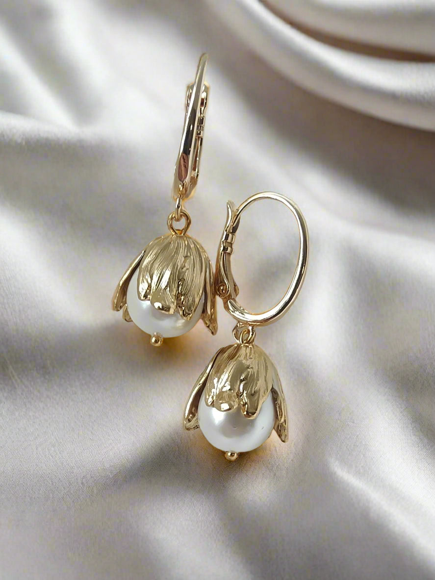 A pair of gold floral pearl drop earrings with a hinged design, featuring a gold post stud attachment and ivory-colored pearl drops.