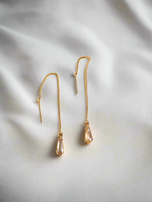 A pair of gold-plated threader earrings with a crystal pendant, displayed against a white fabric background.