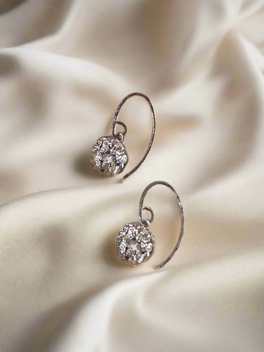 Pair of silver earrings with clear gemstones on a beige fabric background